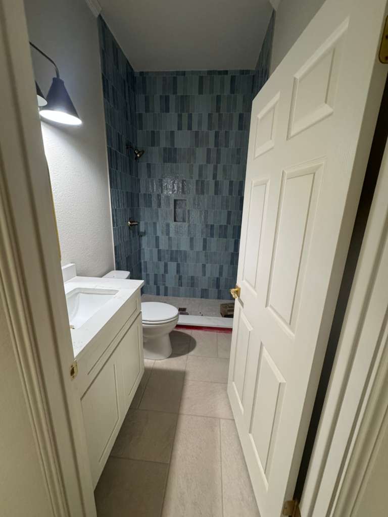 Baño con ducha revestida en azulejo azul y piso claro
